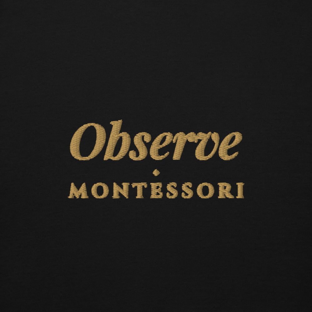 Observe Embroidered Hoodie in Black, close-up of the front embroidery.